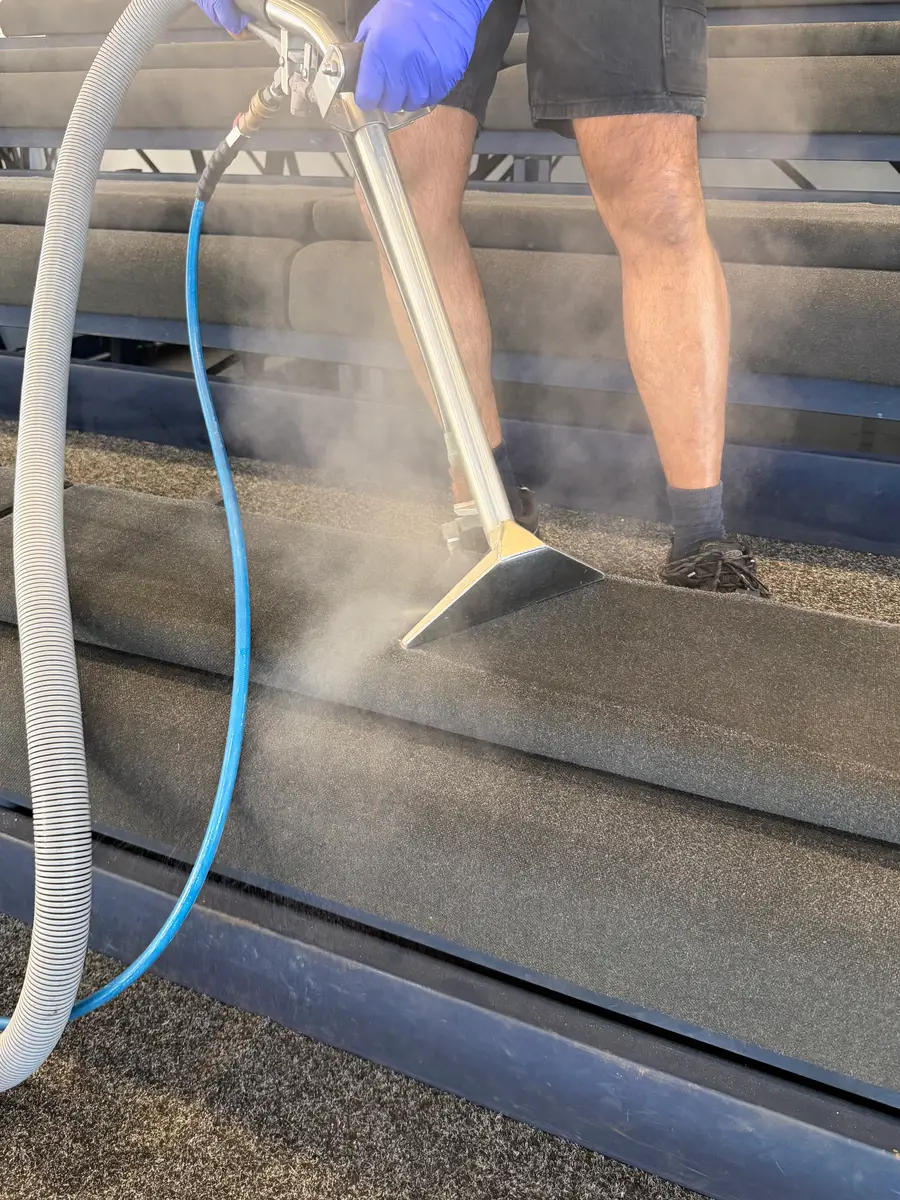 ApexClean steam-cleaning the carpeted steps of tiered seating at an Auckland venue, hot-water extraction wand drawing soil out of the tread