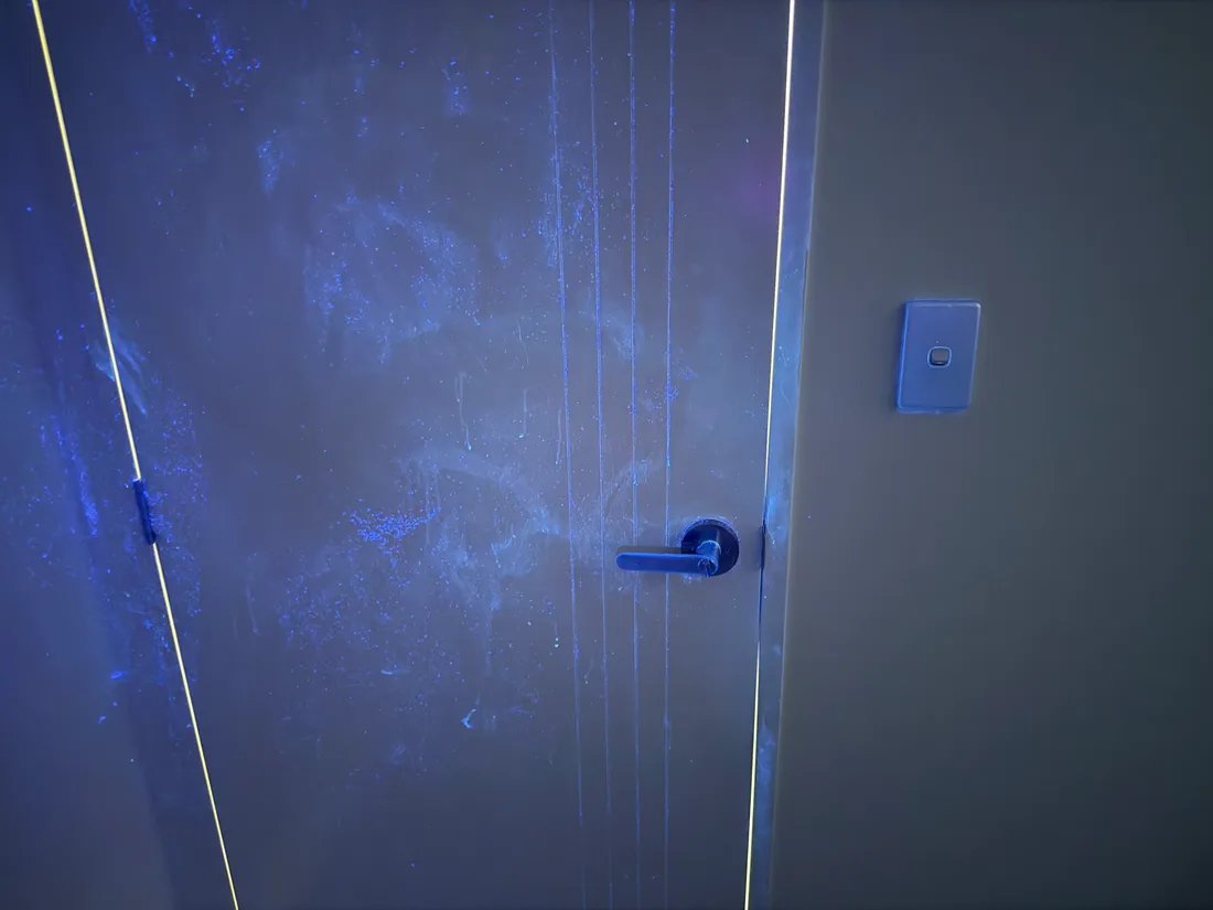 A door under ultraviolet light, splatter marks showing all around and above the handle