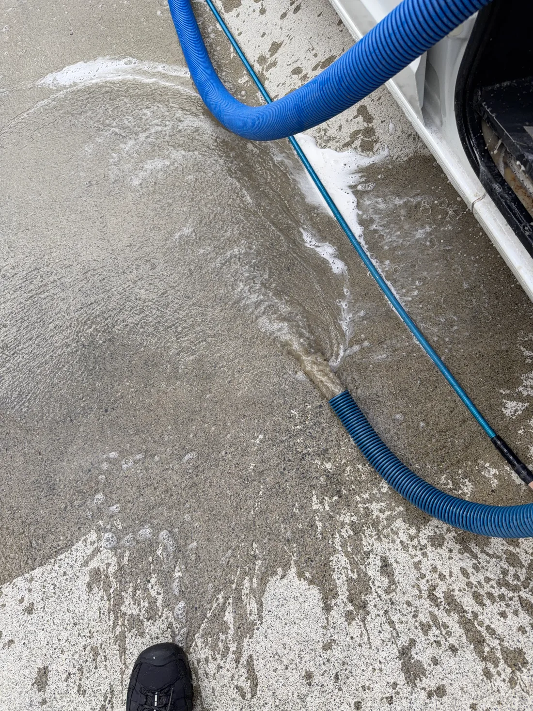 Grey-brown waste water discharging from the extraction tank onto a driveway