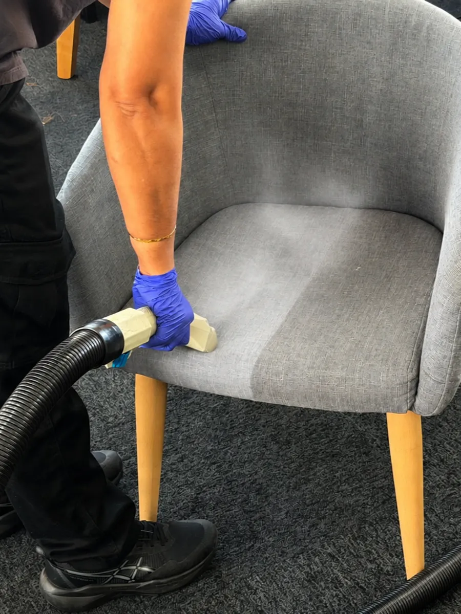 An ApexClean technician steam-cleaning a grey fabric tub chair with a hot-water extraction hand tool in an Auckland home